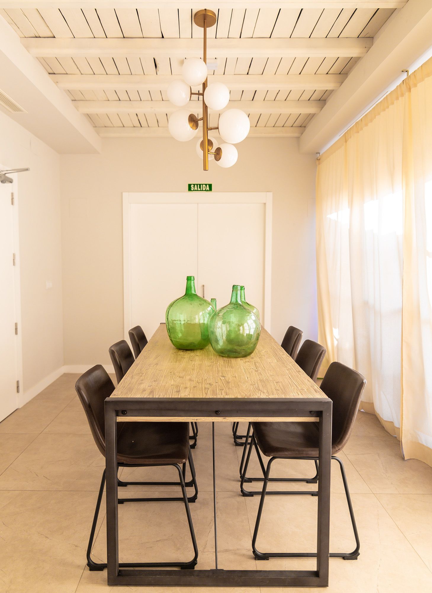 A conference room with a long table, black chairs, a ceiling with wooden beams, and a chandelier.