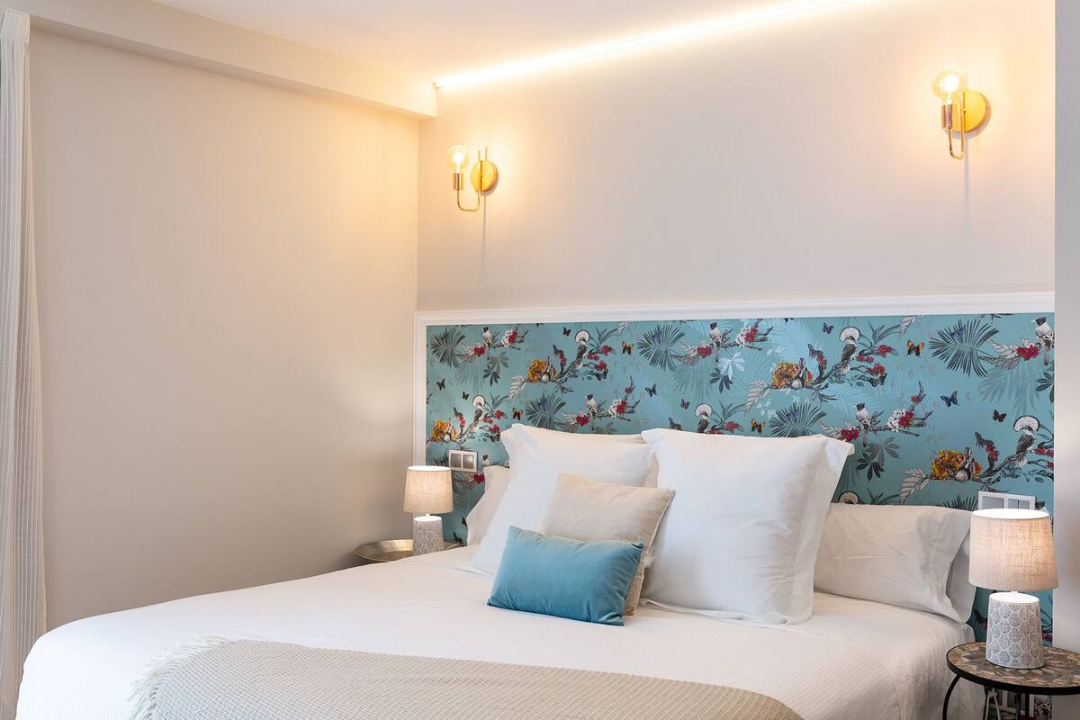 A hotel room with a bed, two wall-mounted lamps, and a floral wallpaper.