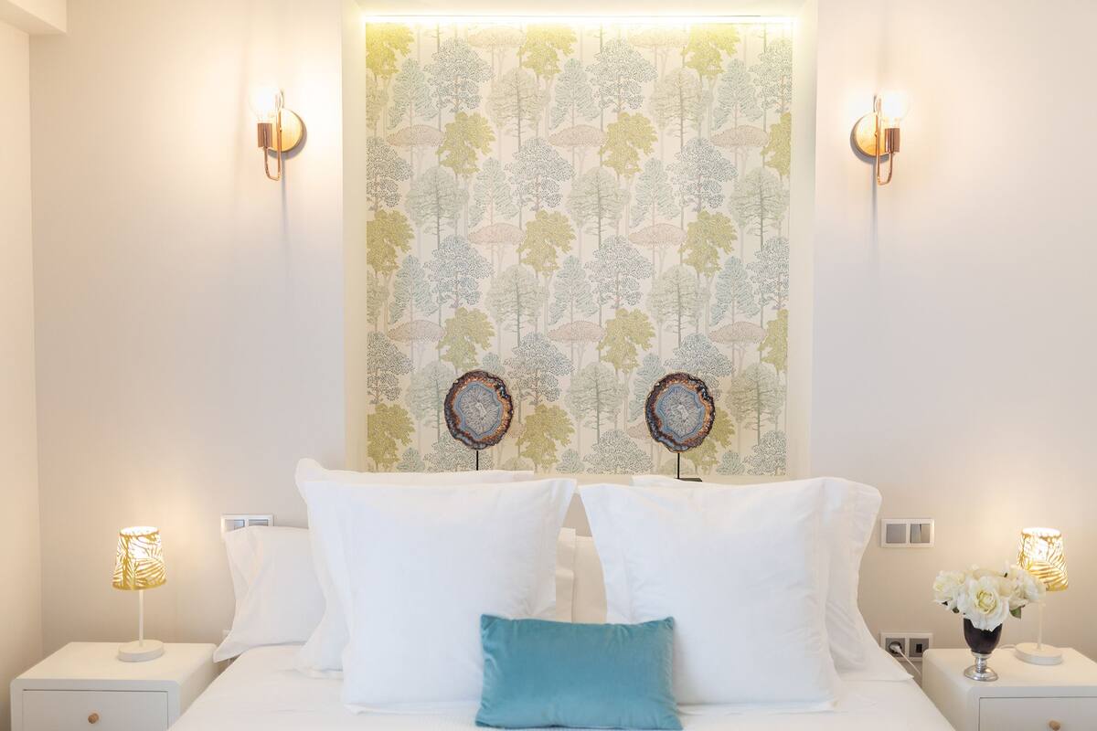 A bedroom with a bed, two wall-mounted light fixtures, and a decorative wall hanging.