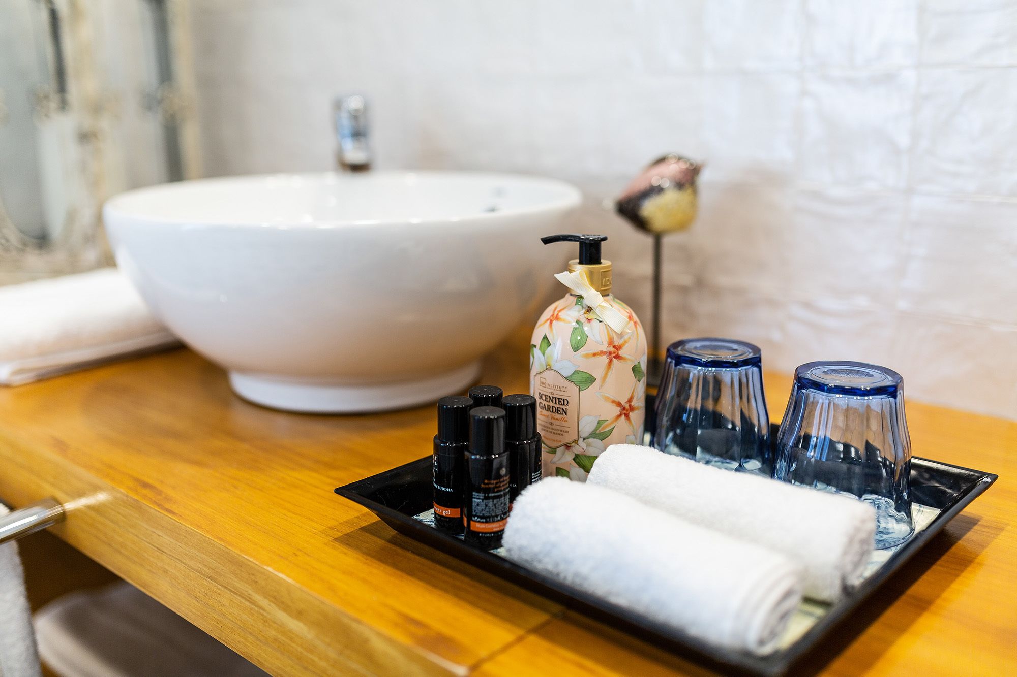 A bathroom sink, a bottle of scented garden hand soap, and two blue glass bottles on a tray.
