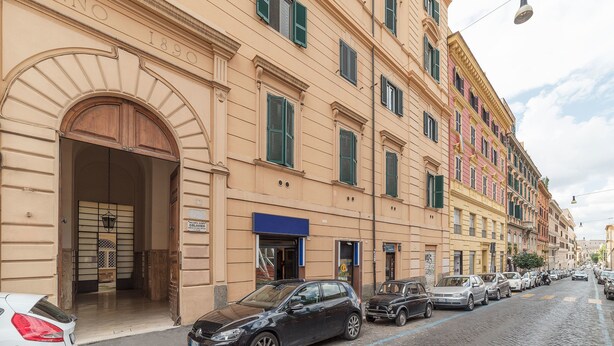 Una hilera de edificios históricos con una calle adoquinada, coches aparcados y cielo despejado.
