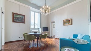Un salón amplio con piso de madera, comedor con mesa y sillas, un sofá azul y una araña.