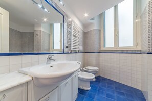 Un baño con un lavamanos blanco, dos inodoros y un espejo grande.