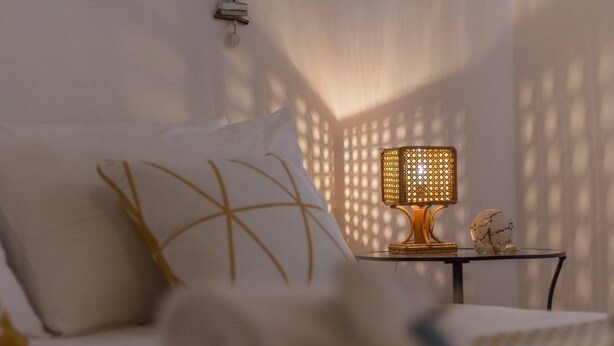 A bed with white bedding and a decorative pillow, a small table with a rattan lamp, and a decorative globe. - Casa Gaia DX (Porto Cesareo)