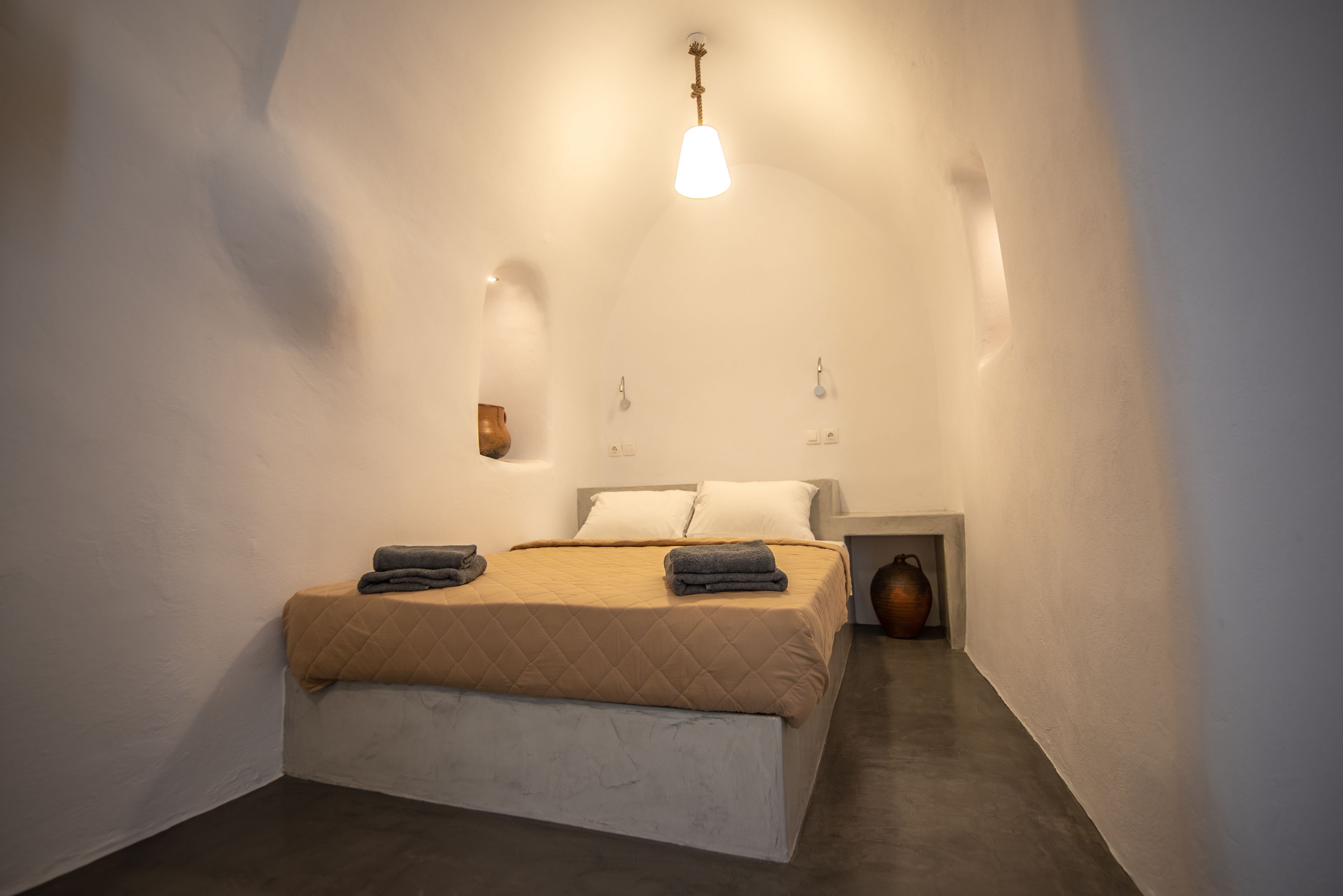 Un dormitorio con cama, mesitas de noche y una lámpara fijada a la pared.