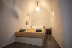 A bedroom with a bed, bedside tables, and a wall-mounted light fixture. - Caves 1880 (Santorini)
