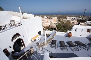 A rooftop terrace with white buildings, a stone wall, and a view of the sea. - Caves 1880 (Santorini)
