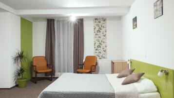A hotel room with a bed, two chairs, a potted plant, a radiator, and a wall with a brick pattern.