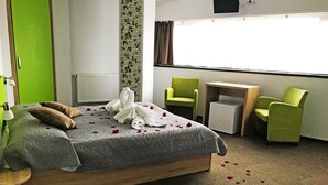 A hotel room with a bed, two green chairs, a small table, and a radiator. - Vila William's (Brasov)