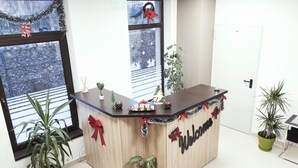 A reception desk with a 'Welcome' sign, potted plants, and a view of a snowy landscape through the windows. - Vila William's (Brasov)