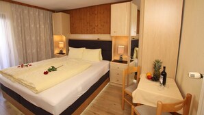 A hotel room with a bed, bedside table, lamp, and a small dining area with a table, chairs, and a fruit basket. - Gästehaus Edelweiss (Soelden)