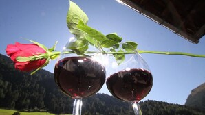 Two wine glasses filled with red wine, a red rose, and green leaves against a mountainous backdrop. - Gästehaus Edelweiss (Soelden)