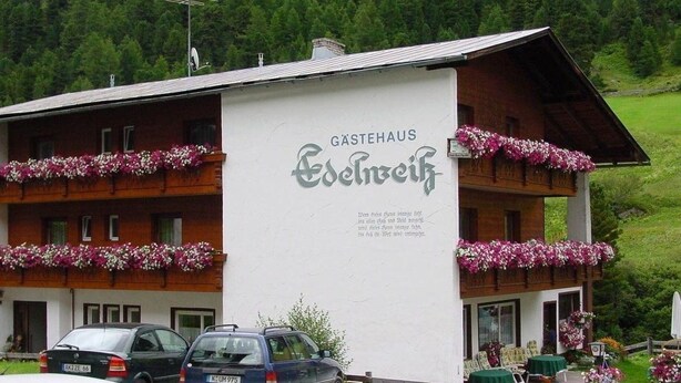 A Gastehaus building with balconies adorned with flowers, a sign with text, and a car parked in front. - Gästehaus Edelweiss (Soelden)