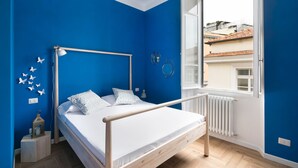 A bedroom with a bed, a window, a radiator, and a view of buildings outside. - Vatican Stylish Apartment (Rome)