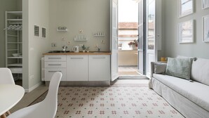 A modern kitchen with white cabinets, a wooden countertop, and a built-in stove. There is a dining area with a white table and chairs, and a living area with a sofa and a coffee table. - Vatican Stylish Apartment (Rome)