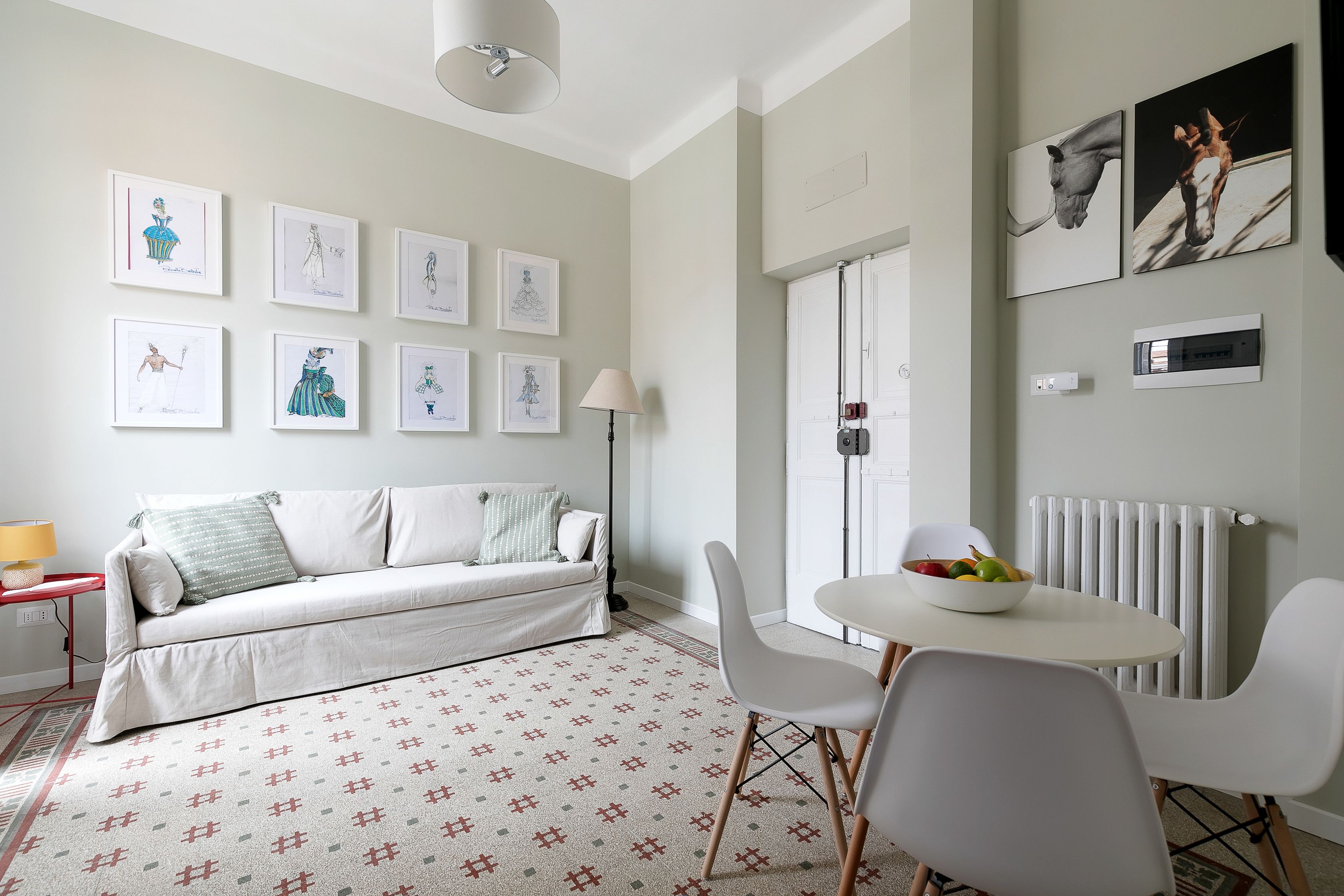 A modern living room with a sofa, chairs, a table with fruit, and framed artwork on the wall.