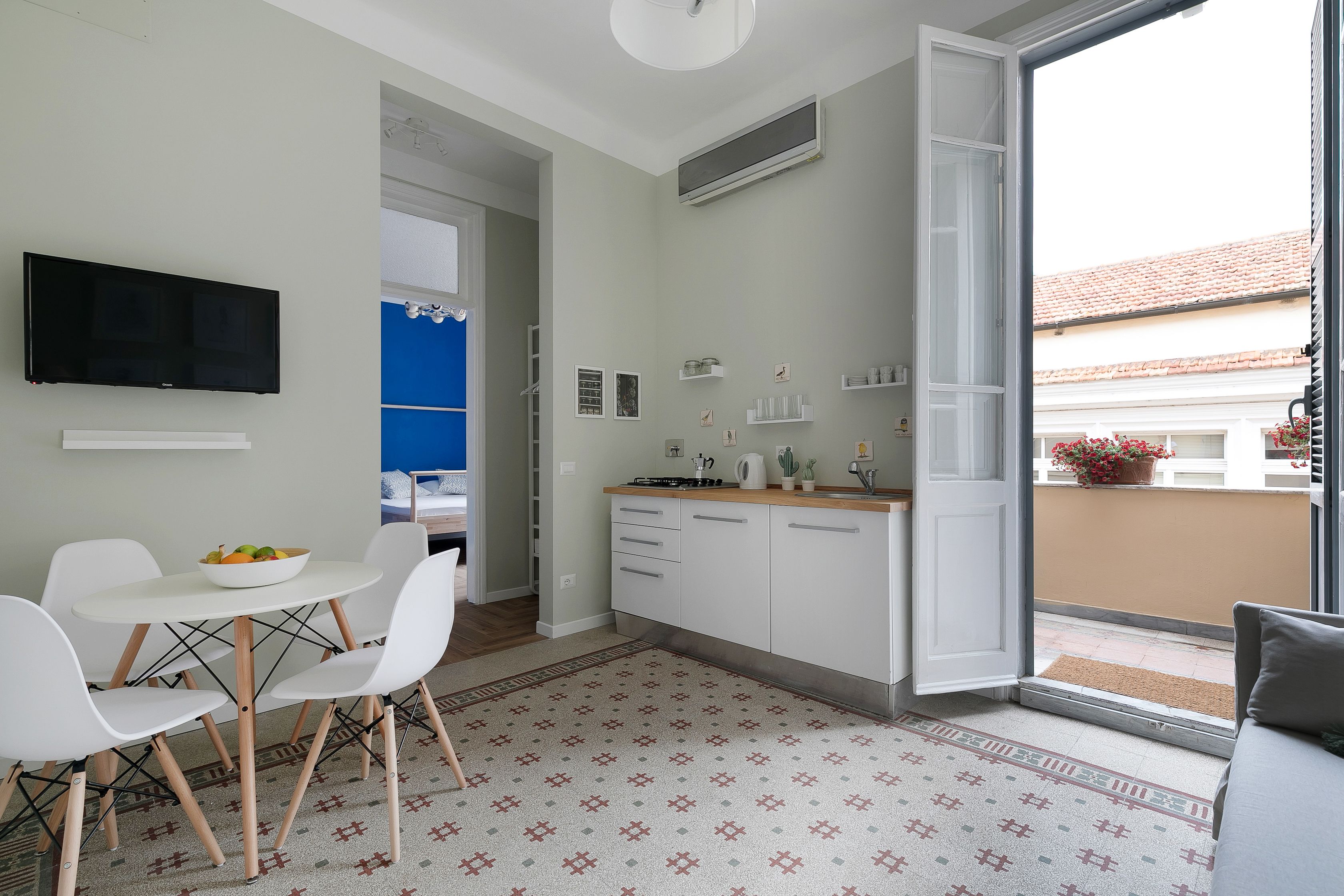 A modern kitchen with white cabinets, a dining area with a white table and chairs, and a large window with a view of the outside.