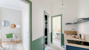 Una cocina moderna con un lavamanos, encimera y estantes. Hay una silla y una lámpara en la habitación contigua.