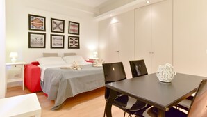 Un dormitorio moderno con cama, mesitas de noche, una mesa de comedor, sillas y una obra de arte en la pared.