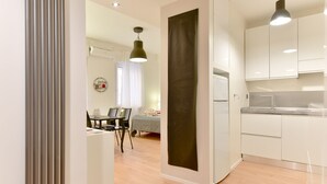 Una cocina moderna con armarios blancos, una obra de arte vertical negra de gran tamaño y un comedor con mesa y sillas.