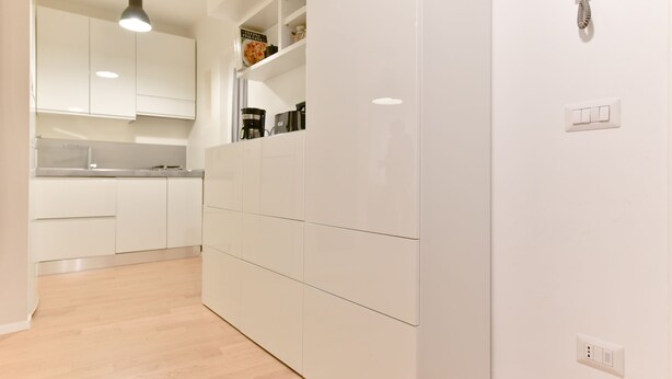 Una cocina moderna con armarios blancos, una lámpara colgante y una cafetera integrada.