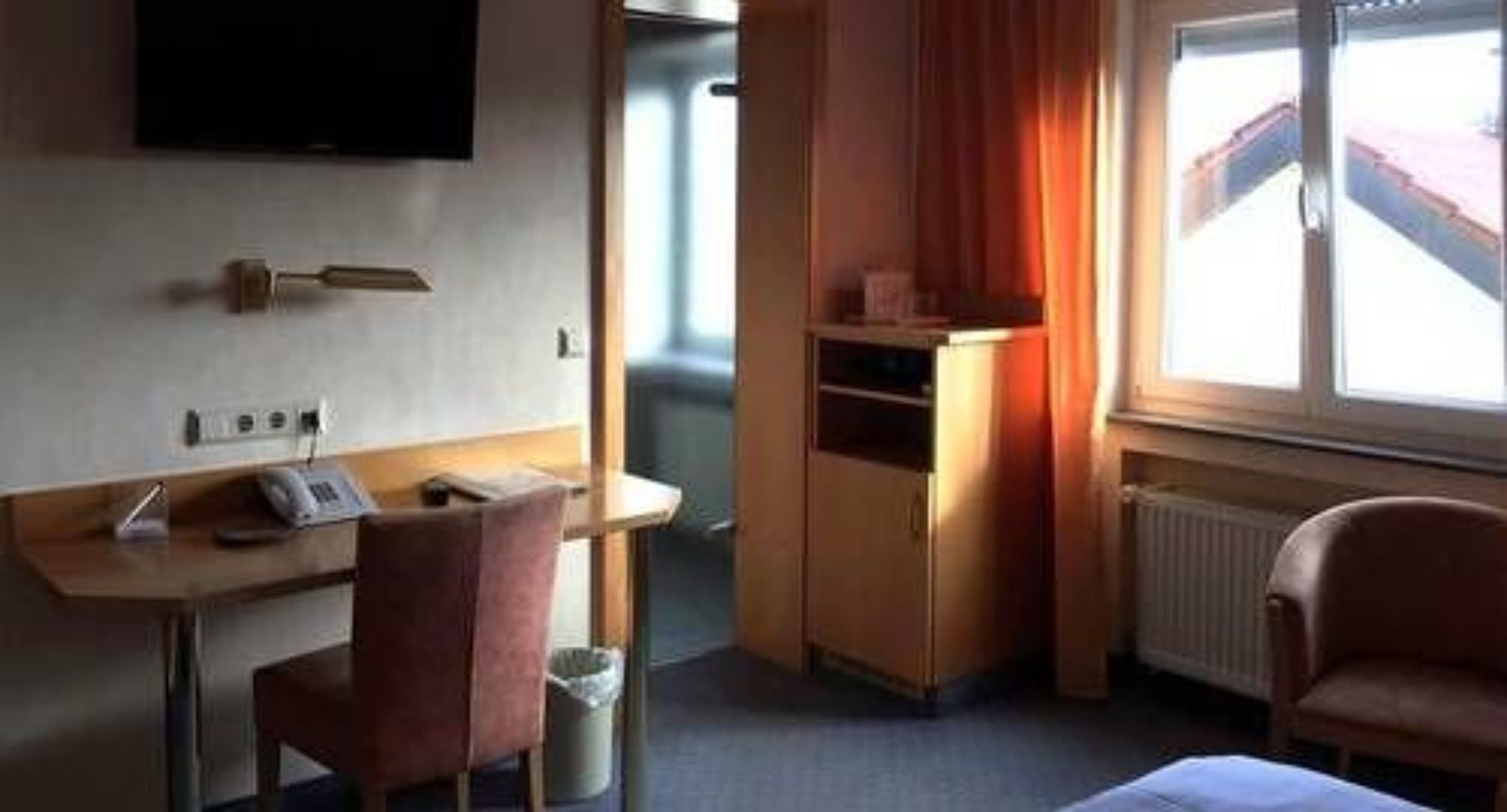 A hotel room with a desk, chair, TV, and a window with curtains.
