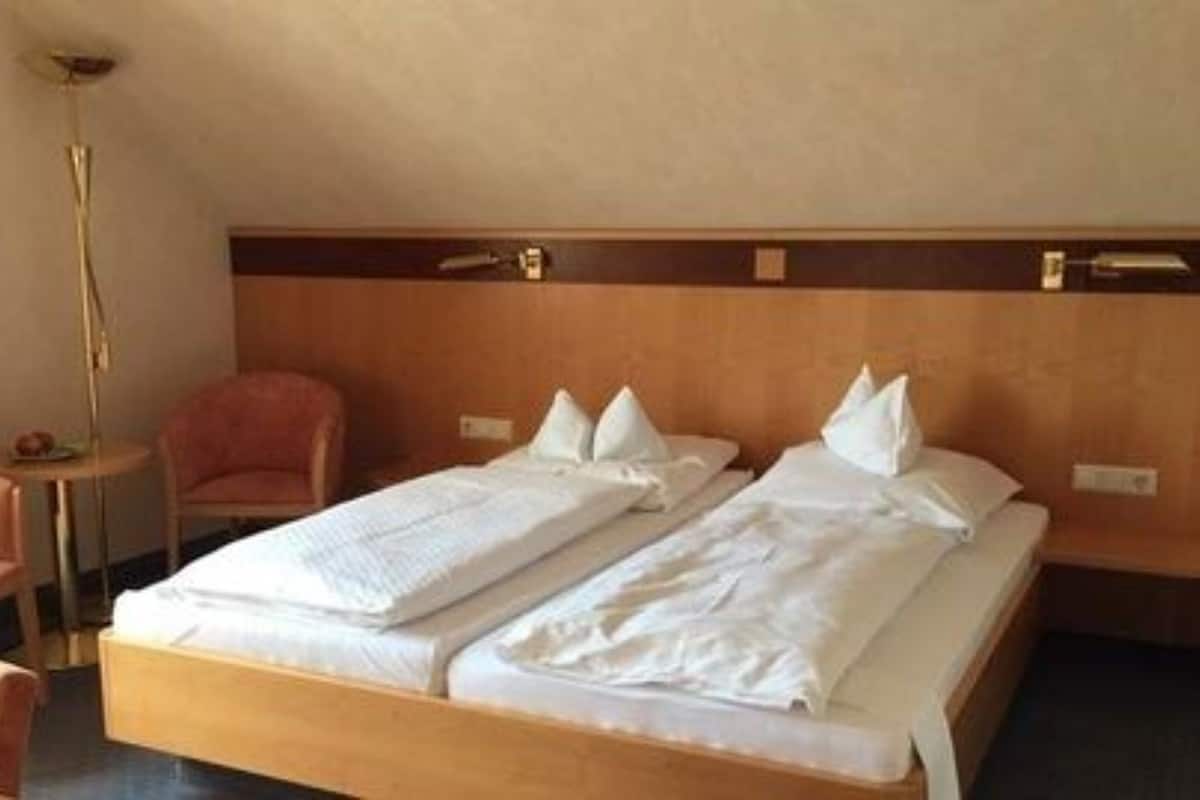 A hotel room with two single beds, a small round table, a chair, and a bedside lamp.
