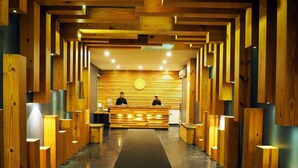 A reception area with a wooden reception desk, two staff members, and a patterned wall in the background. - Raja ka bagh - A Boutique hotel (Nurpur)