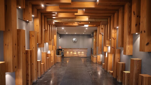 A hotel lobby with a central reception desk, wooden paneling on the walls, and a polished floor. - Raja ka bagh - A Boutique hotel (Nurpur)