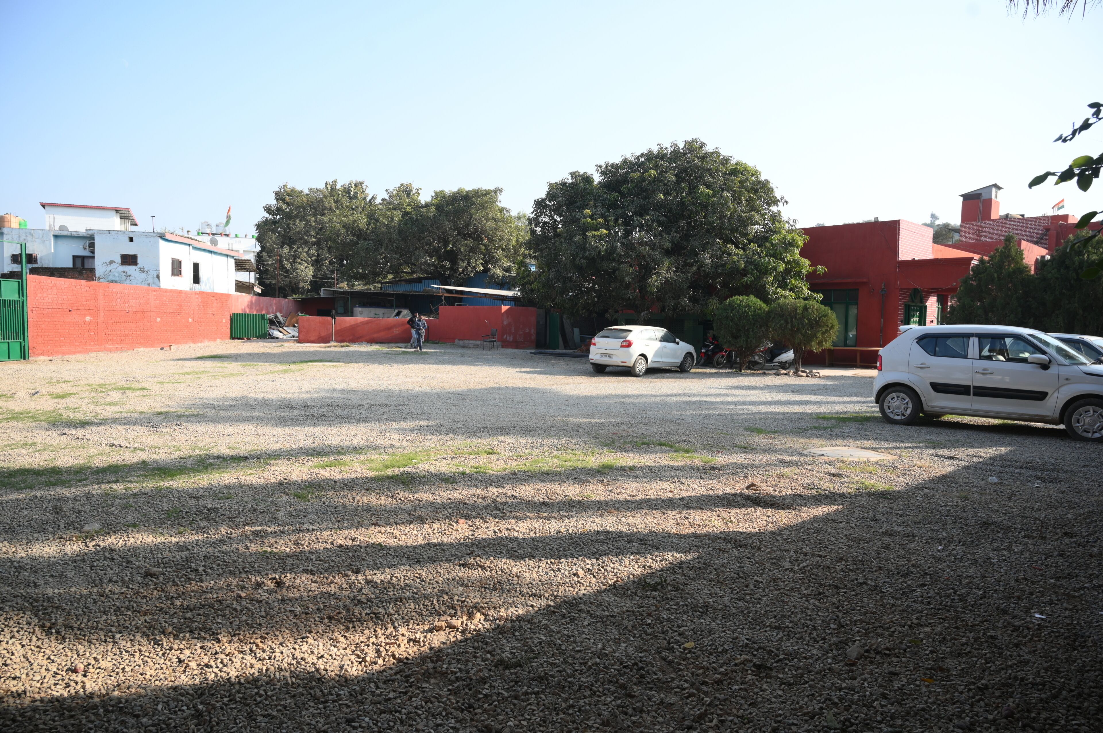 Un aparcamiento con suelo de grava, un coche blanco y un edificio rojo al fondo.