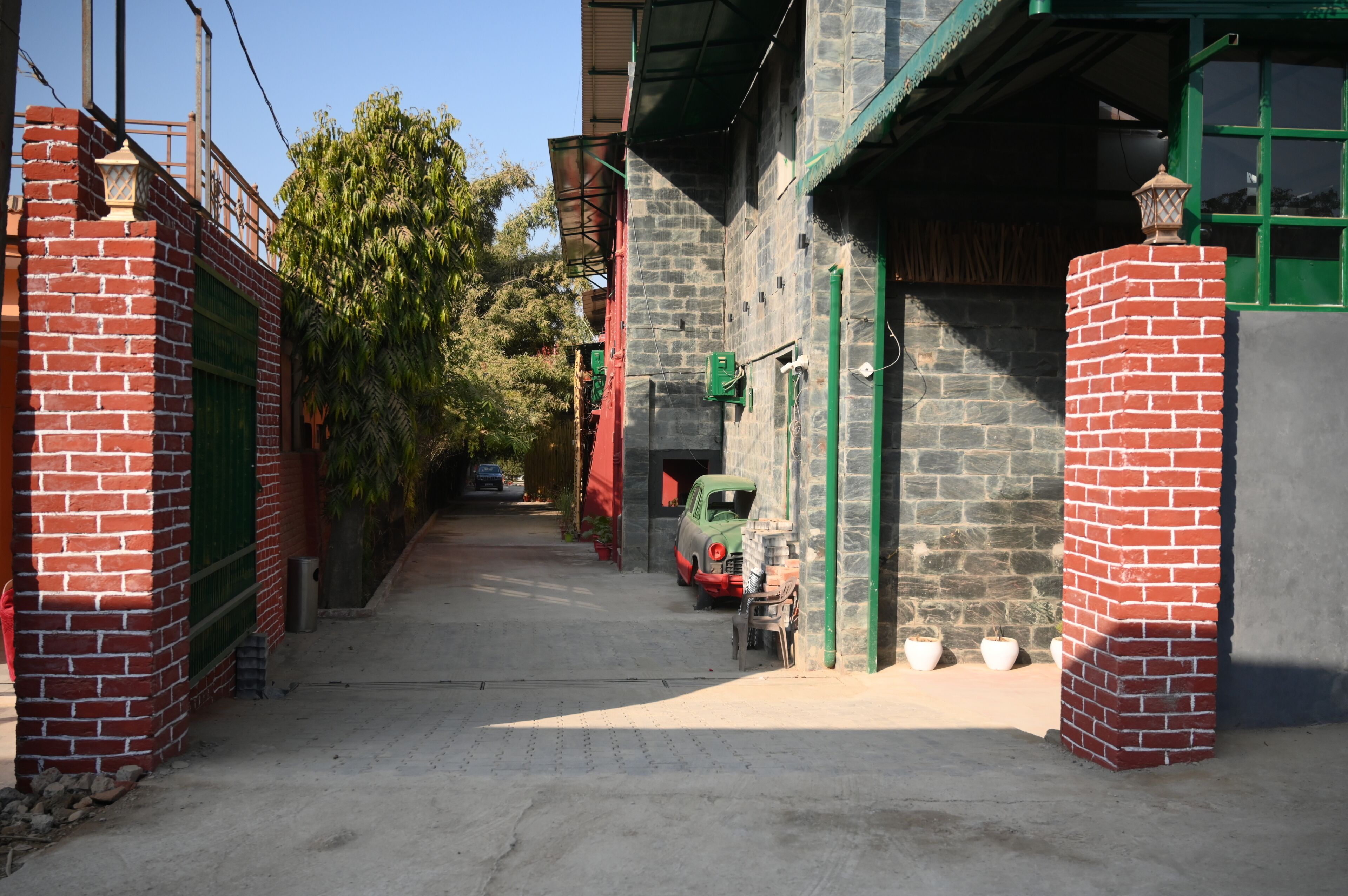 A narrow alleyway with a parked car, brick walls, and a green gate.