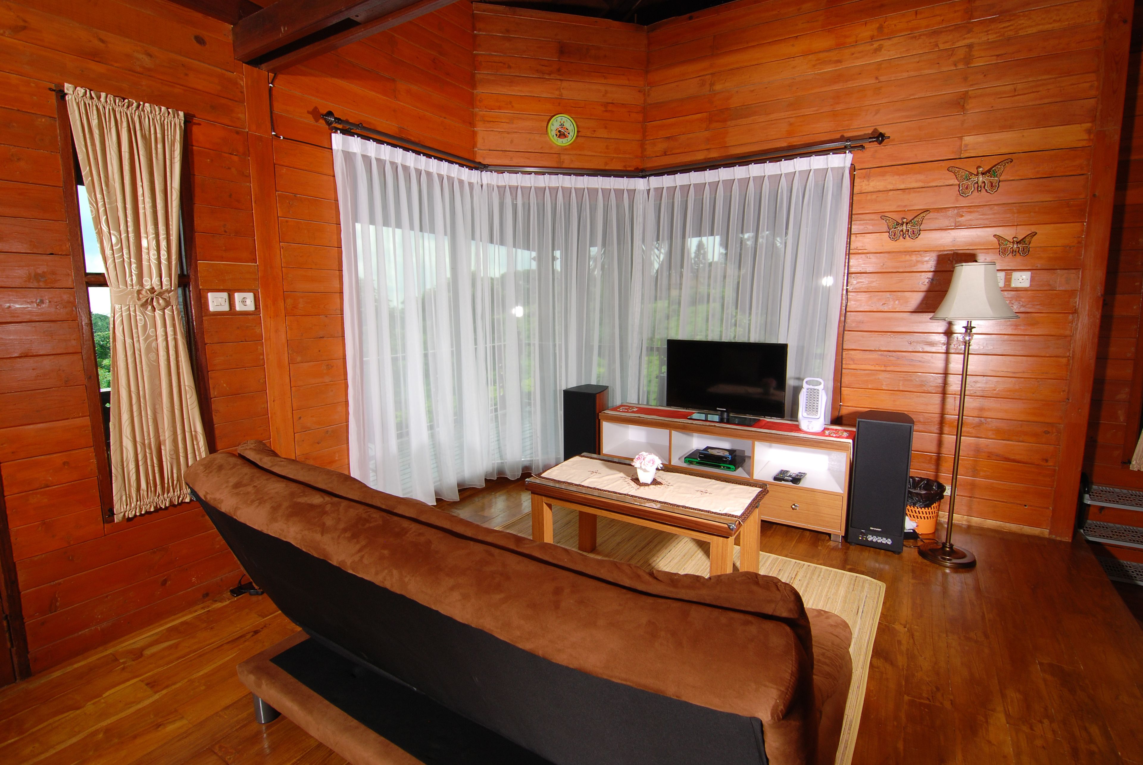 A cozy cabin-style room with a wooden interior, a sofa, a television, and a small table with a lamp.
