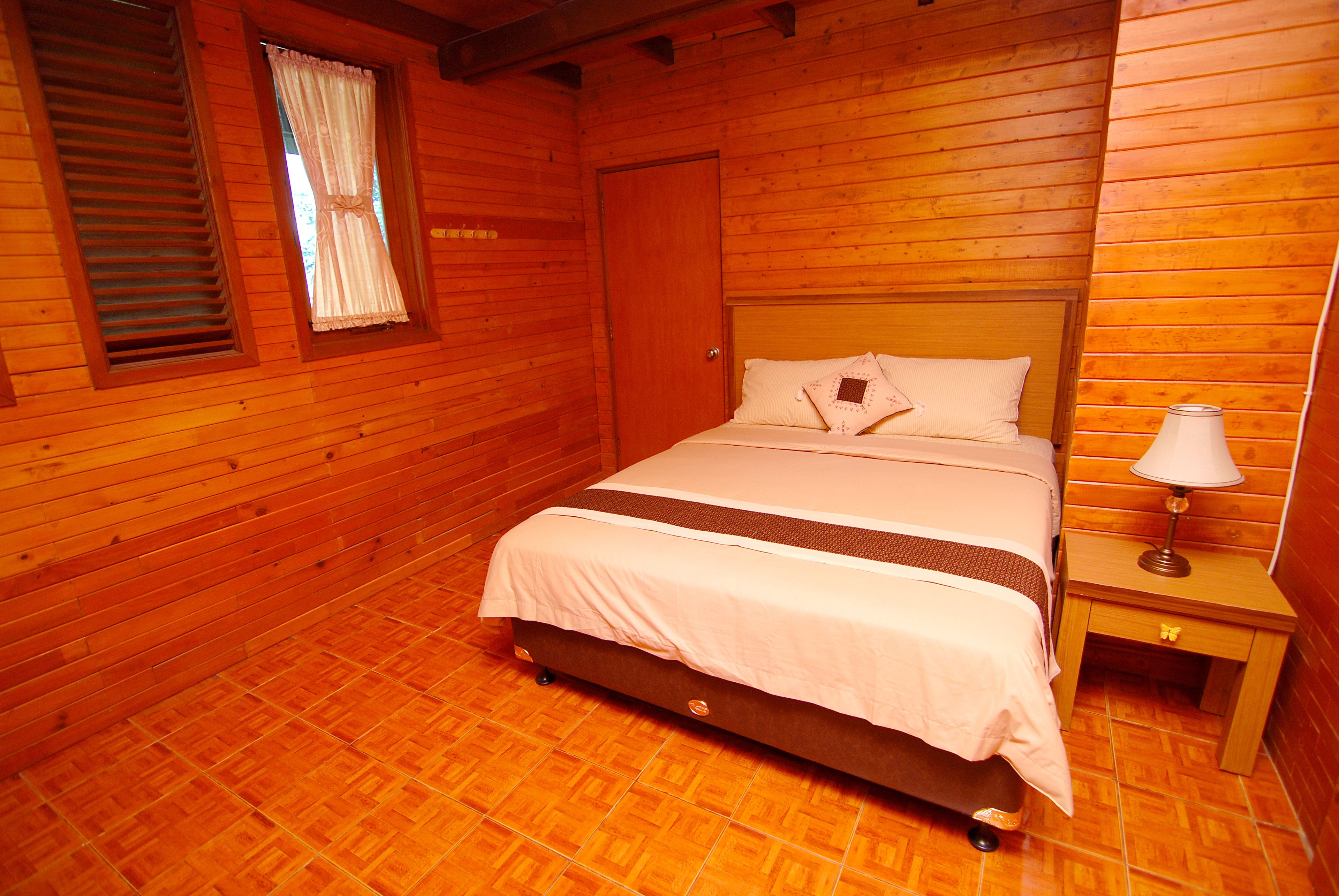 Una habitación de madera con una cama, una mesita de noche y una ventana con cortinas.