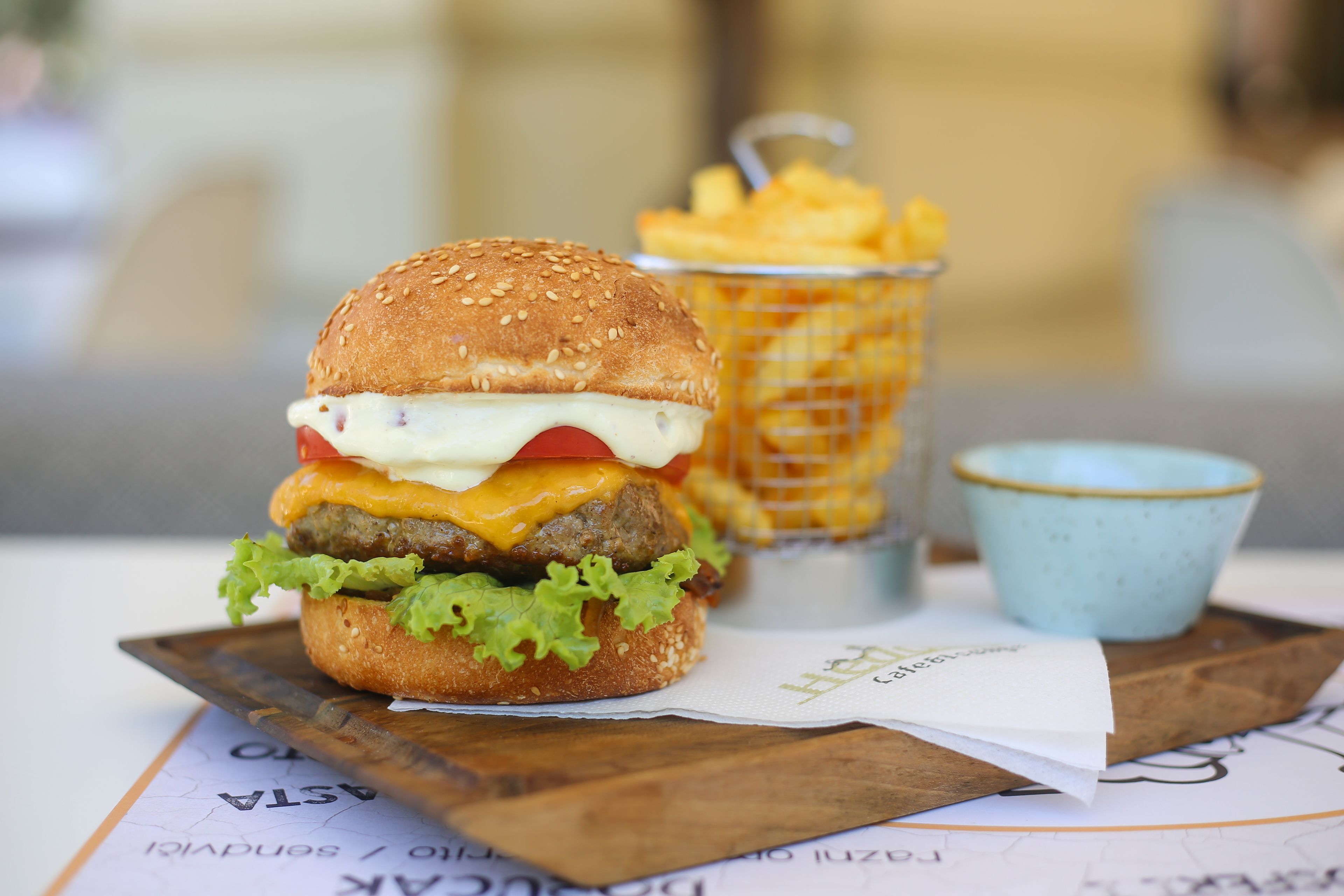 Hamburguesa con papas fritas y una taza pequeña sobre una tabla de madera.