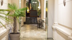 Um saguão de hotel com uma palmeira em vaso, uma mesa de recepção e uma escadaria que leva a um andar superior.