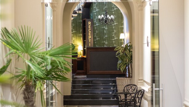 Uma área de recepção com piso de mármore, balcão de atendimento, escada e uma planta em vaso.