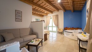 Una habitación con techo de madera, un sofá, una mesa, una bañera y una ventana con cortinas.
