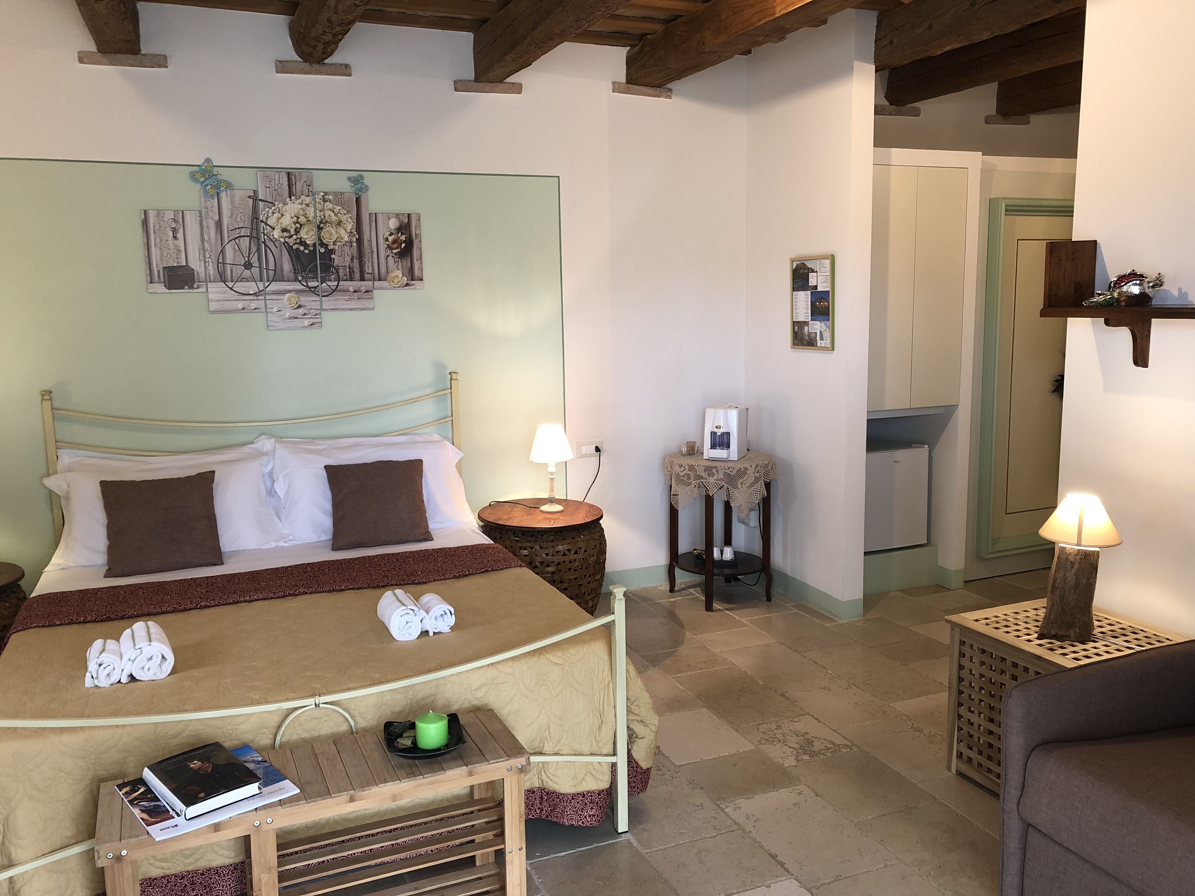 A hotel room with a bed, bedside table, lamp, and a small table with a book and a candle.