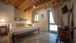 Un dormitorio con una cama de madera, una mesita de noche con lámpara, una silla y un televisor montado en la pared.