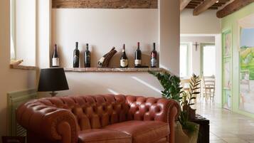 A brown leather sofa, a black lamp, and a wine rack with bottles in a room with wooden beams and a green wall.