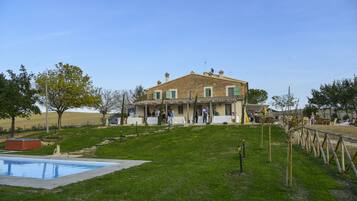 A two-story house with a swimming pool, a grassy yard, and a wooden fence.