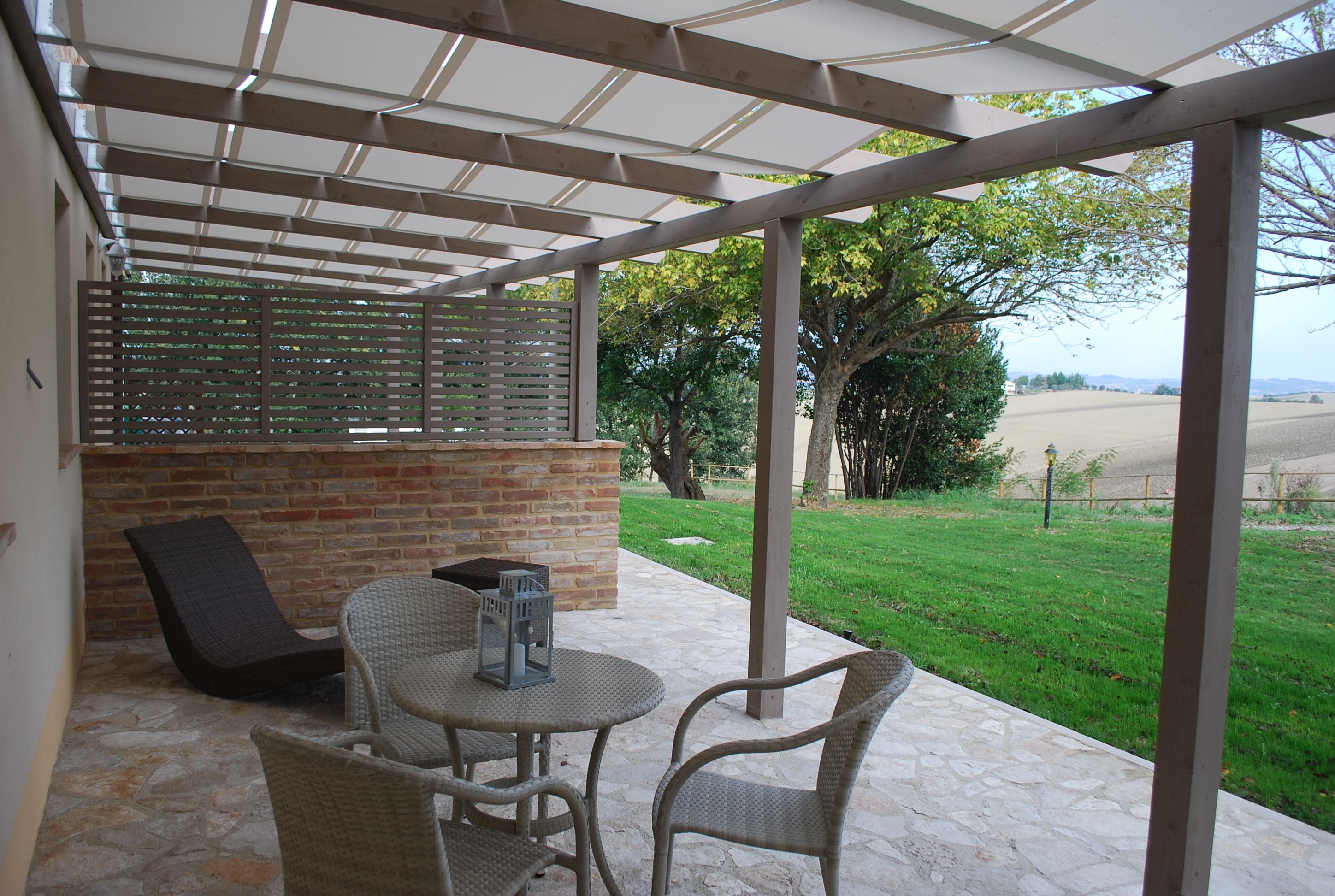 A covered patio area with a brick wall, wicker furniture, and a view of a grassy field.