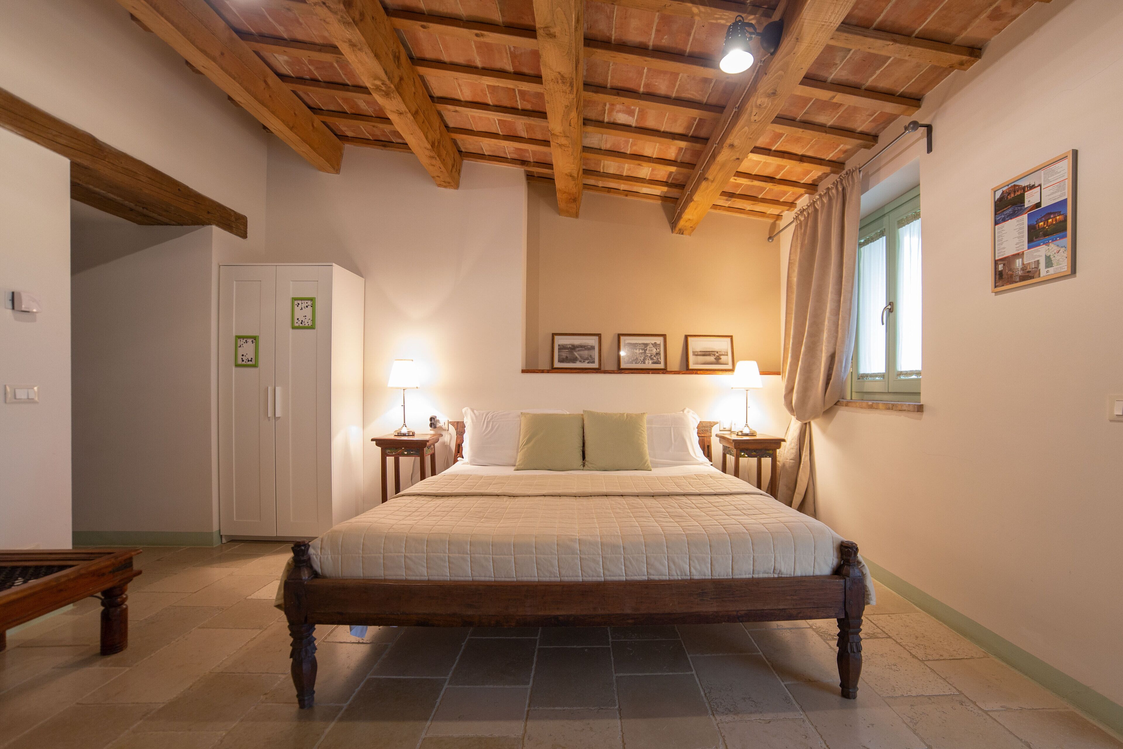 A bedroom with a wooden bed, two bedside tables with lamps, a wardrobe, and a window with curtains.