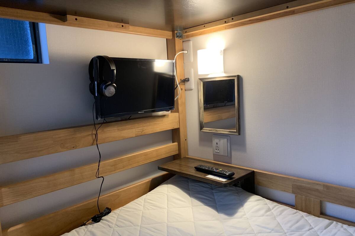 A bunk bed with a television on the upper bunk, a bedside table with a remote control, and a wall-mounted mirror.