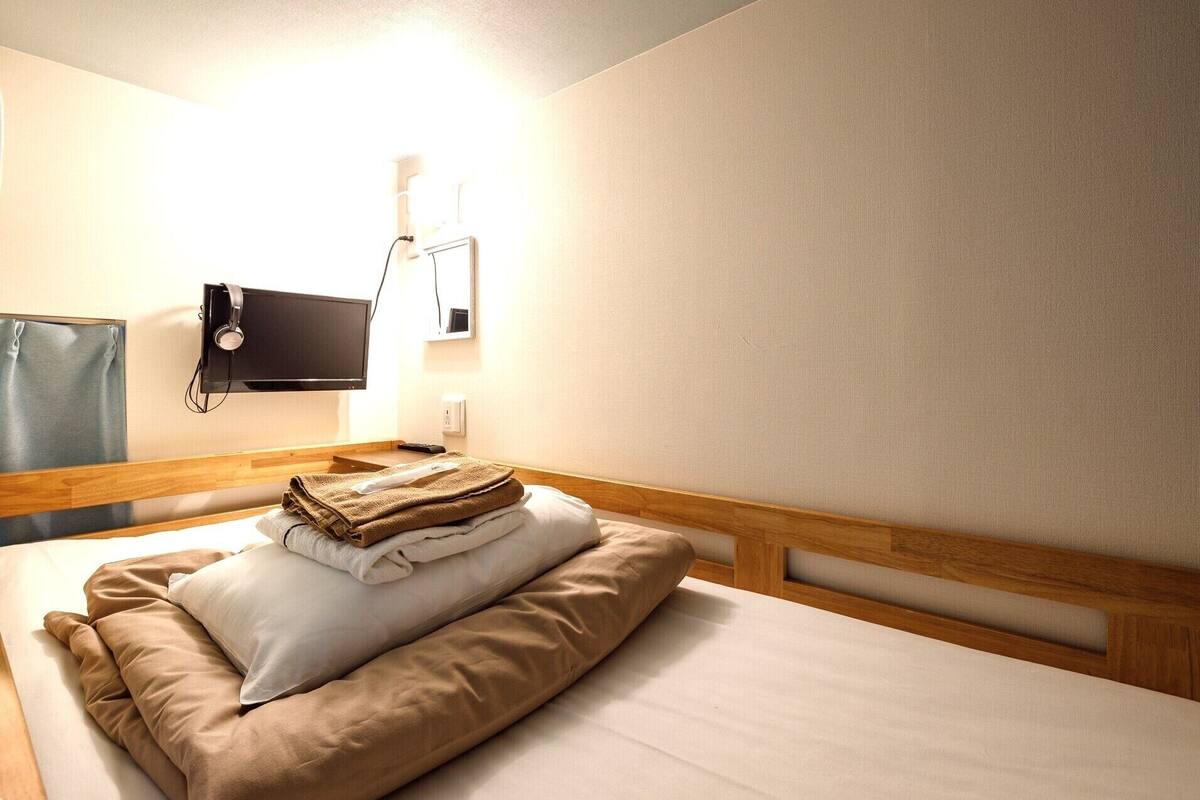 A hotel room with a bed, a TV mounted on the wall, and a bedside table with a lamp.