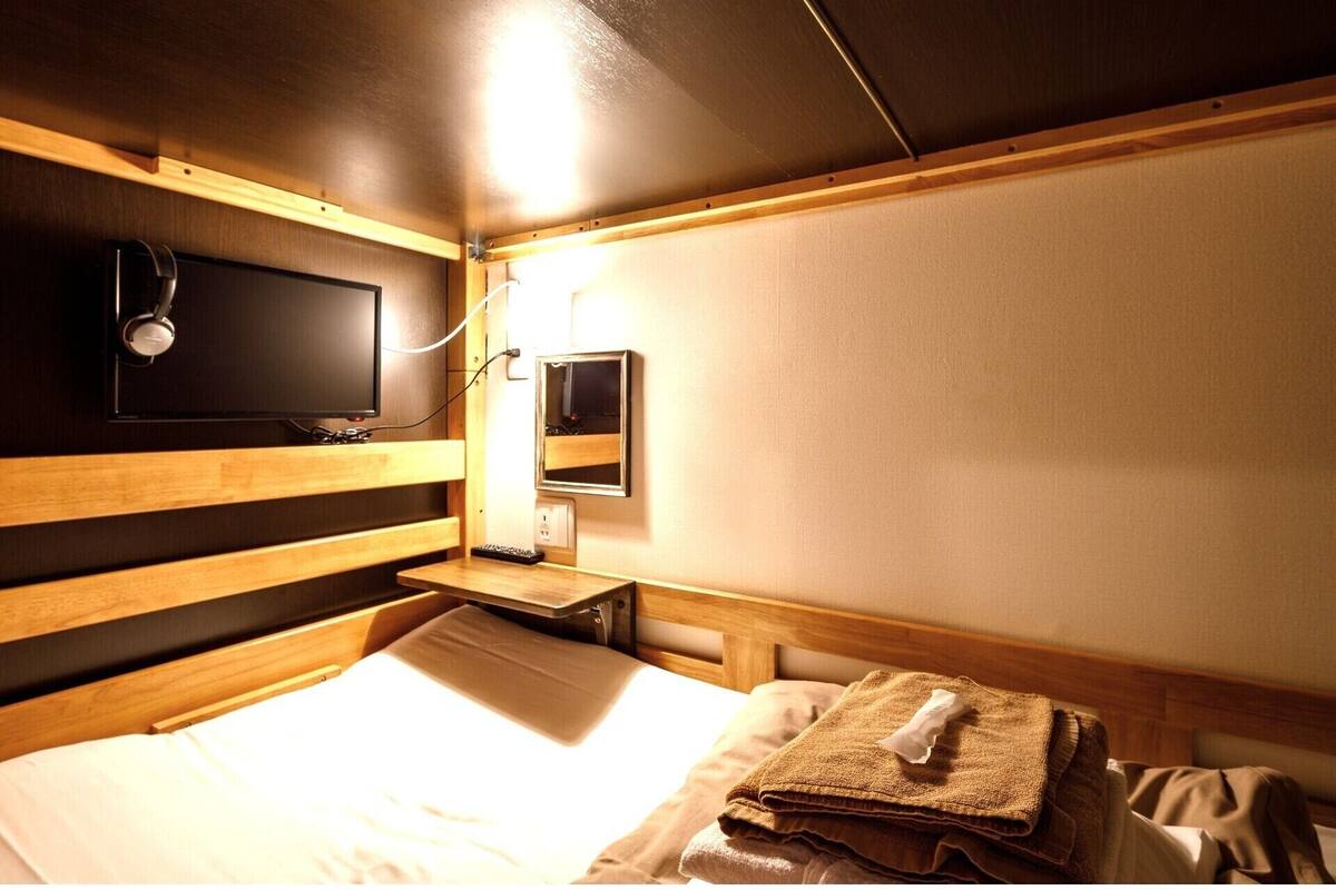 A compact hotel room with a bed, a bedside table, a TV, and a small bedside lamp.