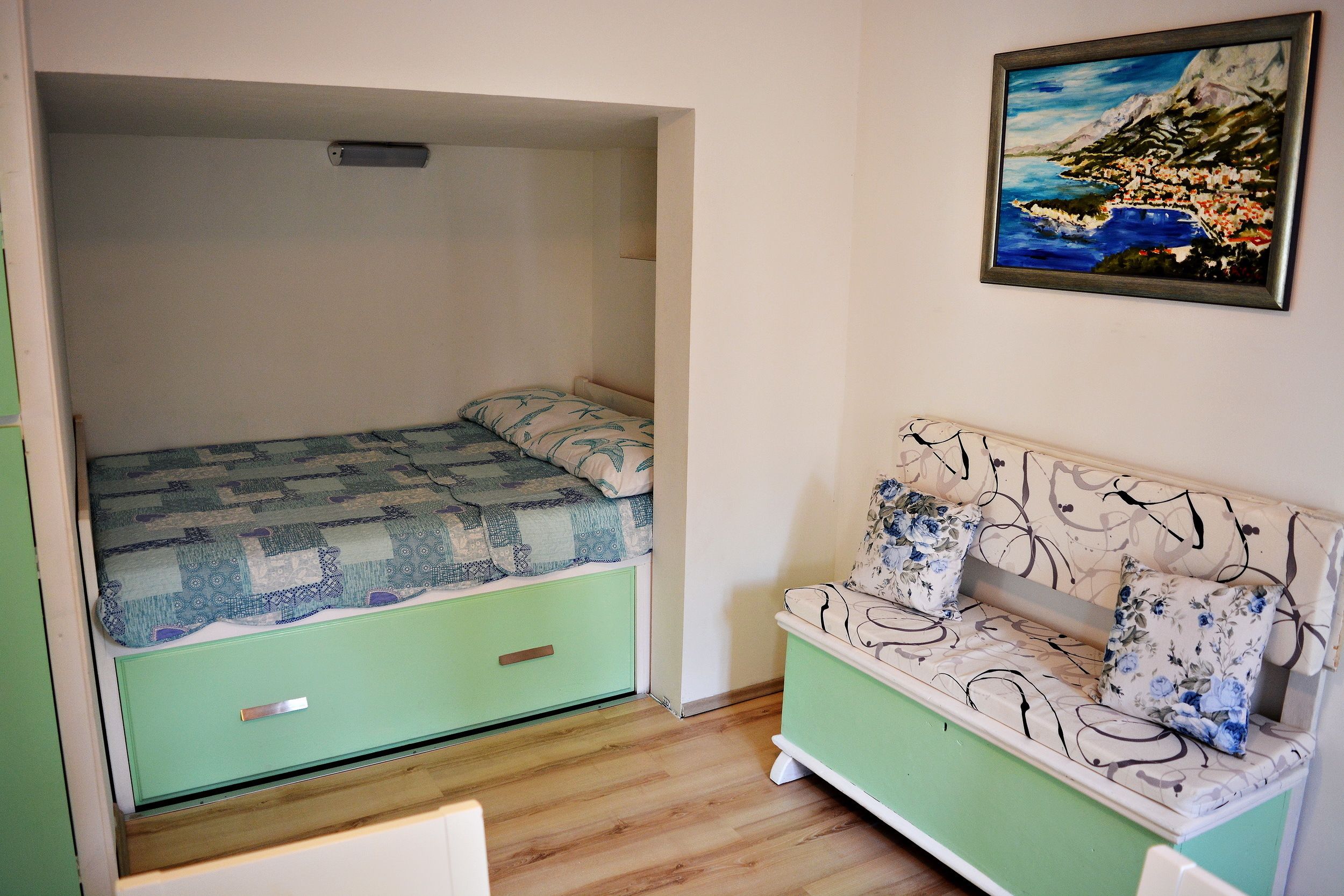 A room with a bed, a green sofa, and a painting on the wall.