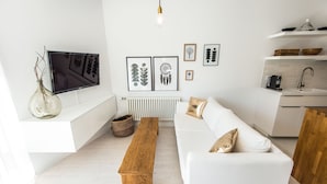 A modern living room with a white sofa, a wooden bench, and a TV mounted on a white wall. - Super-Apartamenty Exotic (Poznan)
