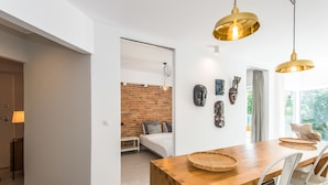 A modern room with a wooden dining table, white chairs, a brick wall, and a bed with a white headboard. - Super-Apartamenty Exotic (Poznan)
