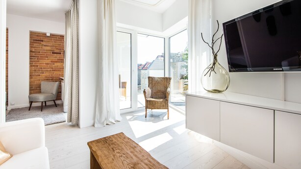 A modern living room with a large TV, a wooden coffee table, a wicker chair, and a view through a glass door to the outside. - Super-Apartamenty Exotic (Poznan)